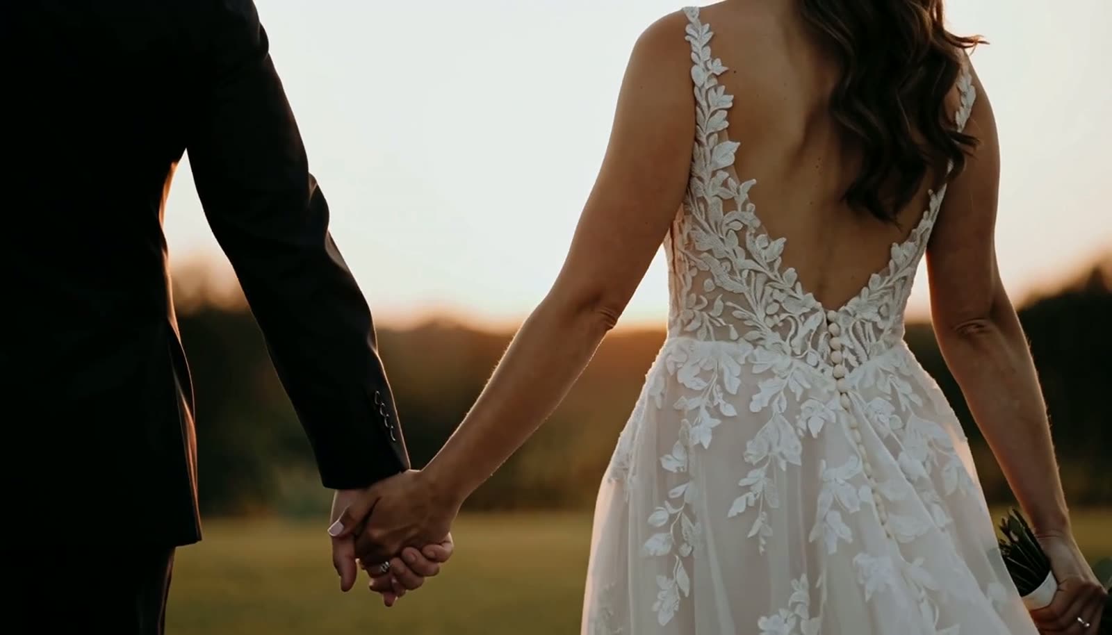 Novios tomados de la mano entre pétalos, con luz cálida de atardecer